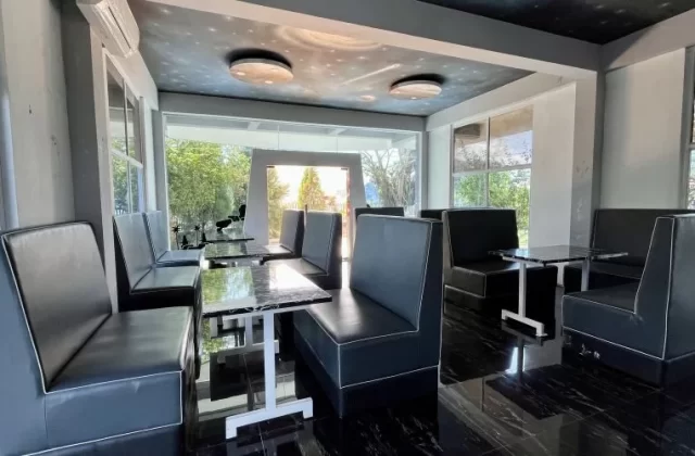 A modern restaurant interior with black booth seating, marble-top tables, dark tiled floor, large windows, and a space-themed ceiling.