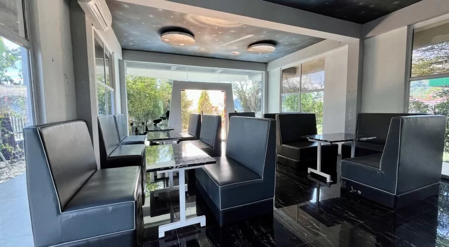 A modern restaurant interior with black booth seating, marble-top tables, dark tiled floor, large windows, and a space-themed ceiling.
