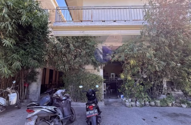 Sacca Restaurant's light-colored exterior with a balcony is framed by lush green bamboo and potted plants. Motorbikes are parked on the paved area.