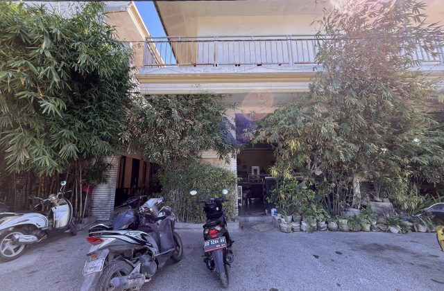 Sacca Restaurant's light-colored exterior with a balcony is framed by lush green bamboo and potted plants. Motorbikes are parked on the paved area.