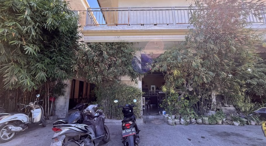 Sacca Restaurant's light-colored exterior with a balcony is framed by lush green bamboo and potted plants. Motorbikes are parked on the paved area.