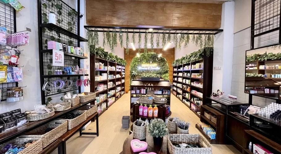 A brightly lit skincare store interior features dark wooden shelves packed with colorful products, wicker baskets, and a green wall with a neon sign at the back.
