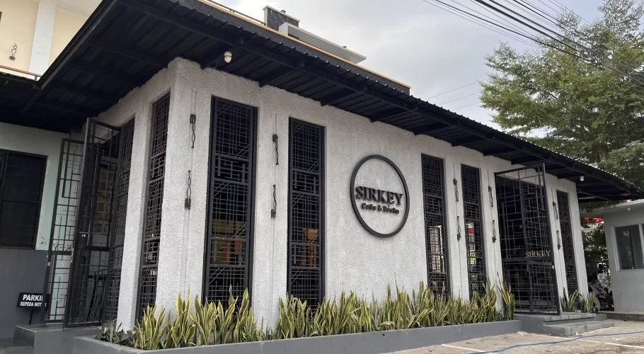 The modern white exterior of Sirkey Cafe & Bistro features black-framed windows, a dark roof, and green plants in a planter under a cloudy sky.