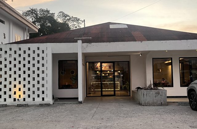 Exterior of Soemba Coffee & Resto in Waikabubak, a white building with a patterned screen, dark roof, and warm interior lighting visible through glass.