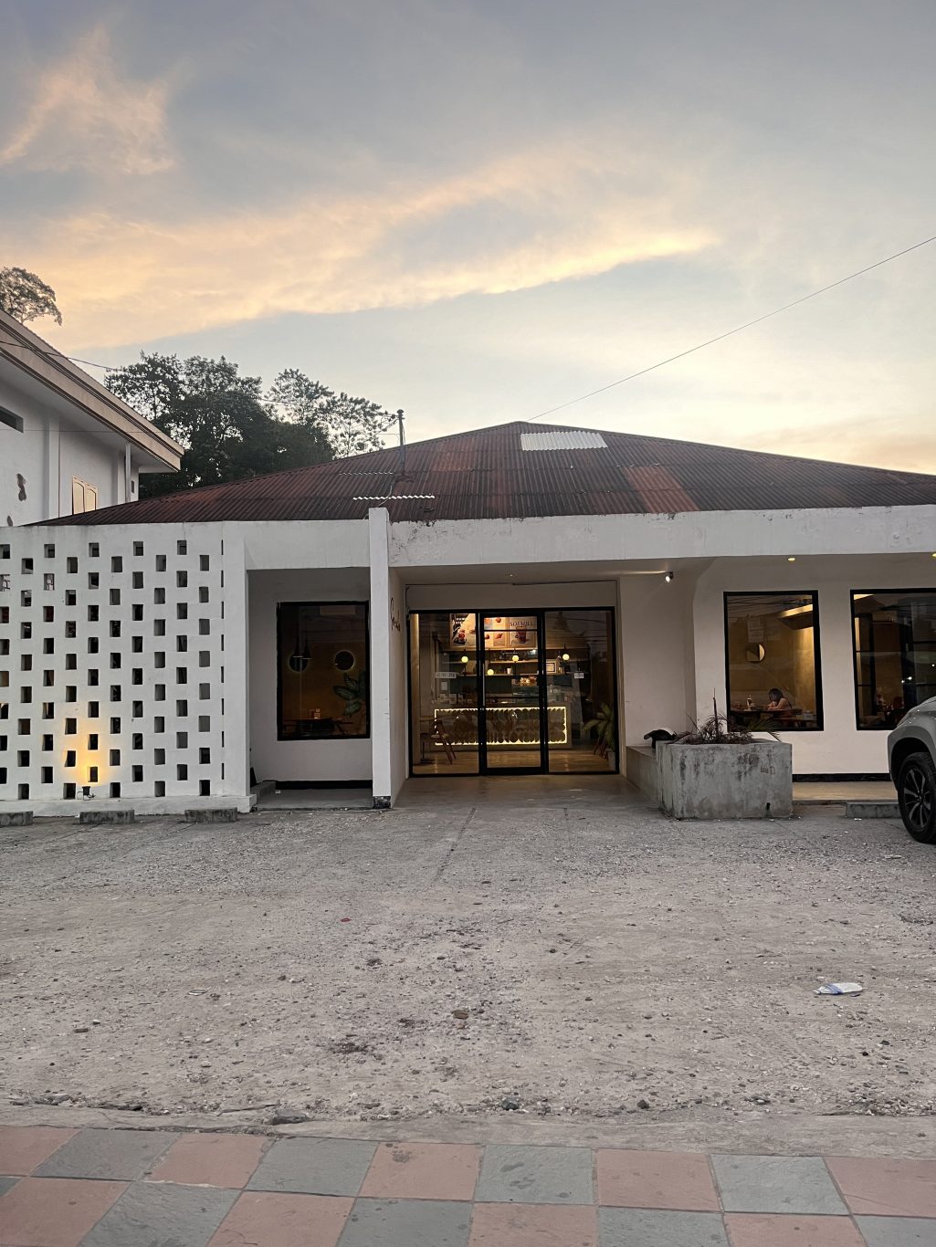 Exterior of Soemba Coffee & Resto in Waikabubak, a white building with a patterned screen, dark roof, and warm interior lighting visible through glass.