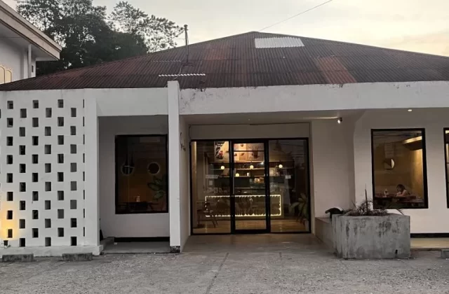 Exterior of Soemba Coffee & Resto in Waikabubak, a white building with a patterned screen, dark roof, and warm interior lighting visible through glass.