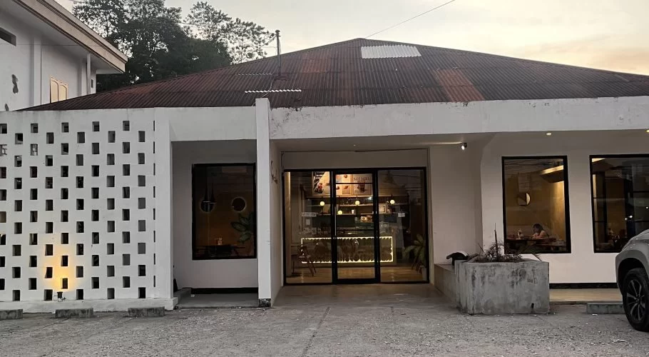 Exterior of Soemba Coffee & Resto in Waikabubak, a white building with a patterned screen, dark roof, and warm interior lighting visible through glass.