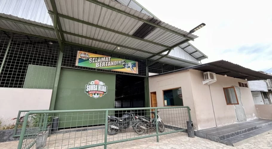 Sumba Hijau Futsal building's green entrance, displaying a "Selamat Bertanding" banner, with two motorcycles parked behind a metal fence.