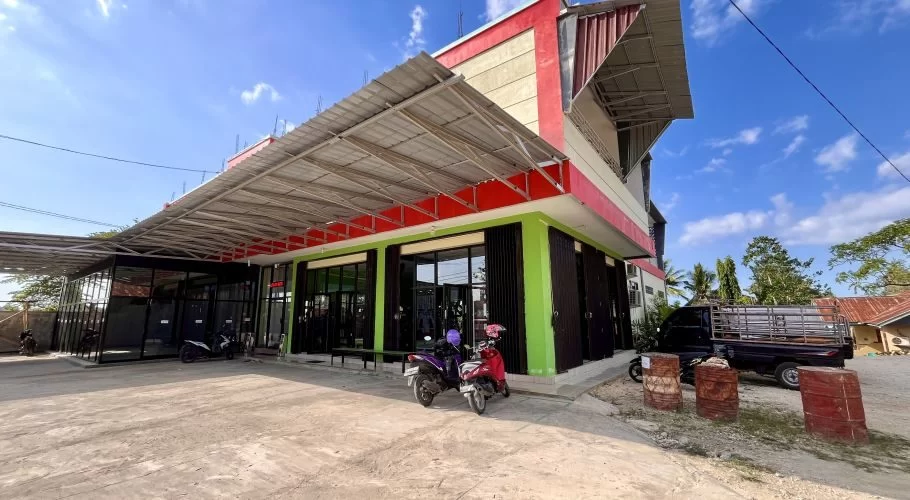 A modern two-story building, Surya Baru Gym, with red, cream, and green walls, glass windows, and a wide metal awning, under a blue sky.