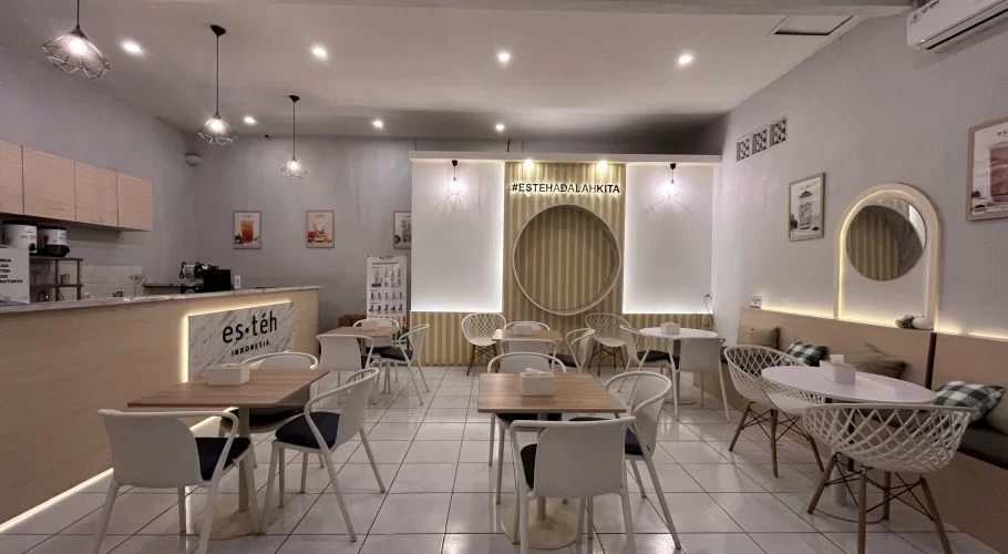 Modern cafe interior with light gray walls, white tiled floors, wooden tables, white chairs, a service counter, and a circular wooden wall design.