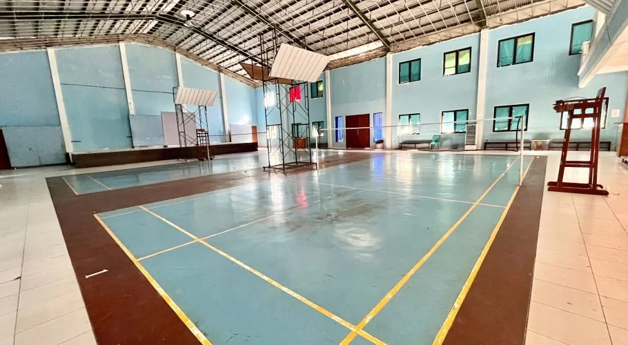 Indoor badminton court in West Sumba with light blue walls, a metal roof, and two blue playing surfaces marked by yellow and brown lines.