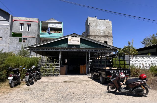 Timoer Cafe, a building with a dark green roof, stands under a clear blue sky with a black pickup truck and motorbikes parked outside.