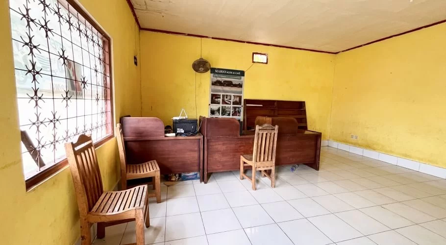 The interior of Travel Mario's office features bright yellow walls, white tiled floors, dark wooden desks, and chairs, with a window on the left.