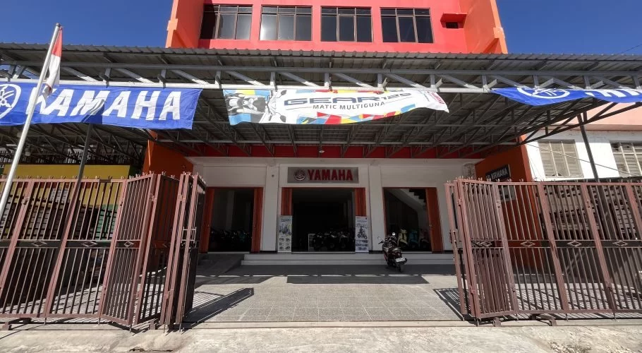 The UD Nirwana Yamaha motorcycle dealership in Waingapu, East Sumba, features an orange building, blue Yamaha banners, and closed brown gates.