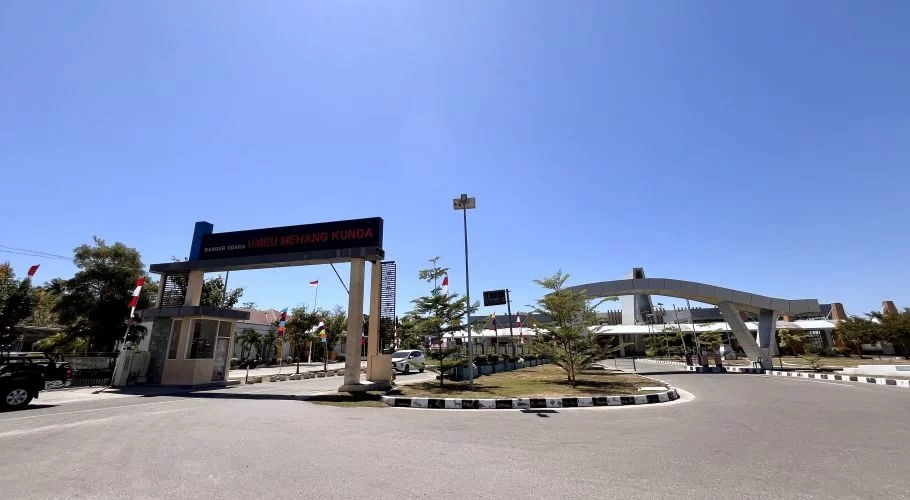 Umbu Mehang Kunda Airport entrance in East Sumba has a large sign, security booth, and modern arched structure under a clear blue sky.