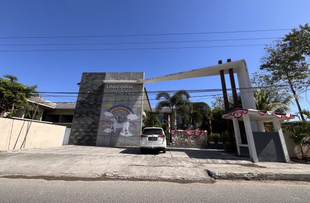 The Unicorn Hotel's grey facade features a colorful unicorn mural and a white car parked in front of its modern entrance under a clear blue sky.