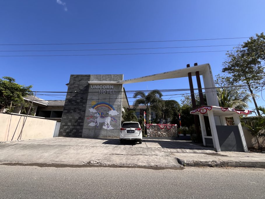 The Unicorn Hotel's grey facade features a colorful unicorn mural and a white car parked in front of its modern entrance under a clear blue sky.