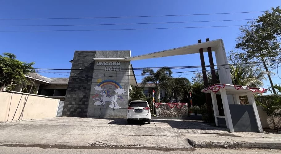 The Unicorn Hotel's grey facade features a colorful unicorn mural and a white car parked in front of its modern entrance under a clear blue sky.
