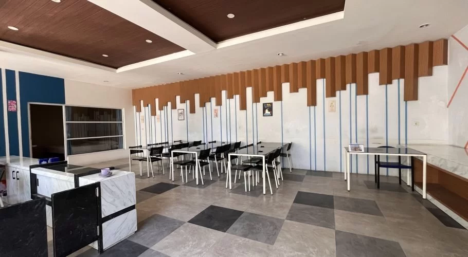 A spacious, modern dining area at Unicorn Hotel features multiple black tables and chairs, white walls with blue stripes and brown panels, and a checkered gray floor.