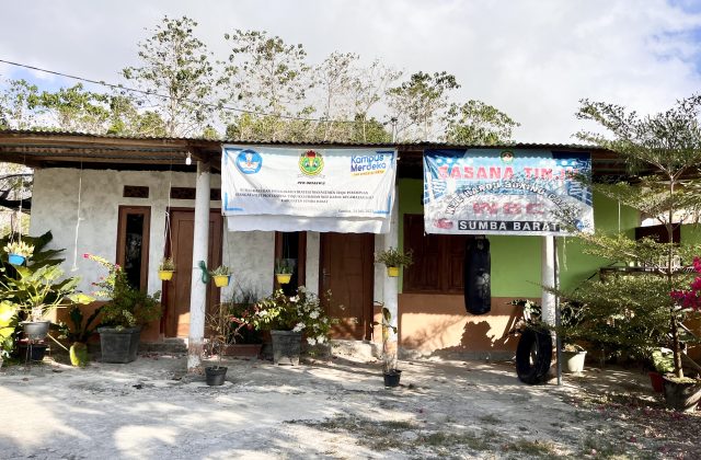 A modest, light-colored building with a corrugated roof displays two banners, one for Wee Karou Boxing Club, and a black punching bag hangs outside.