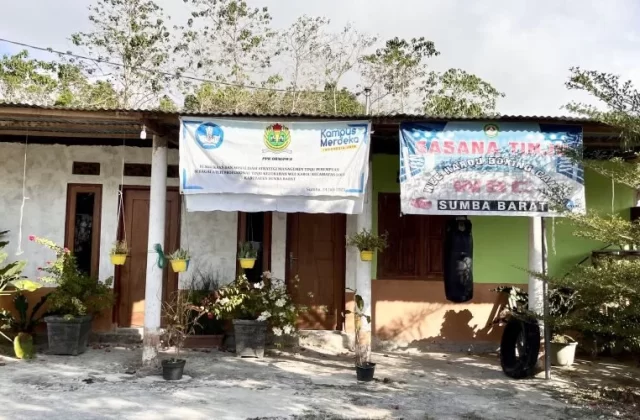 A modest, light-colored building with a corrugated roof displays two banners, one for Wee Karou Boxing Club, and a black punching bag hangs outside.