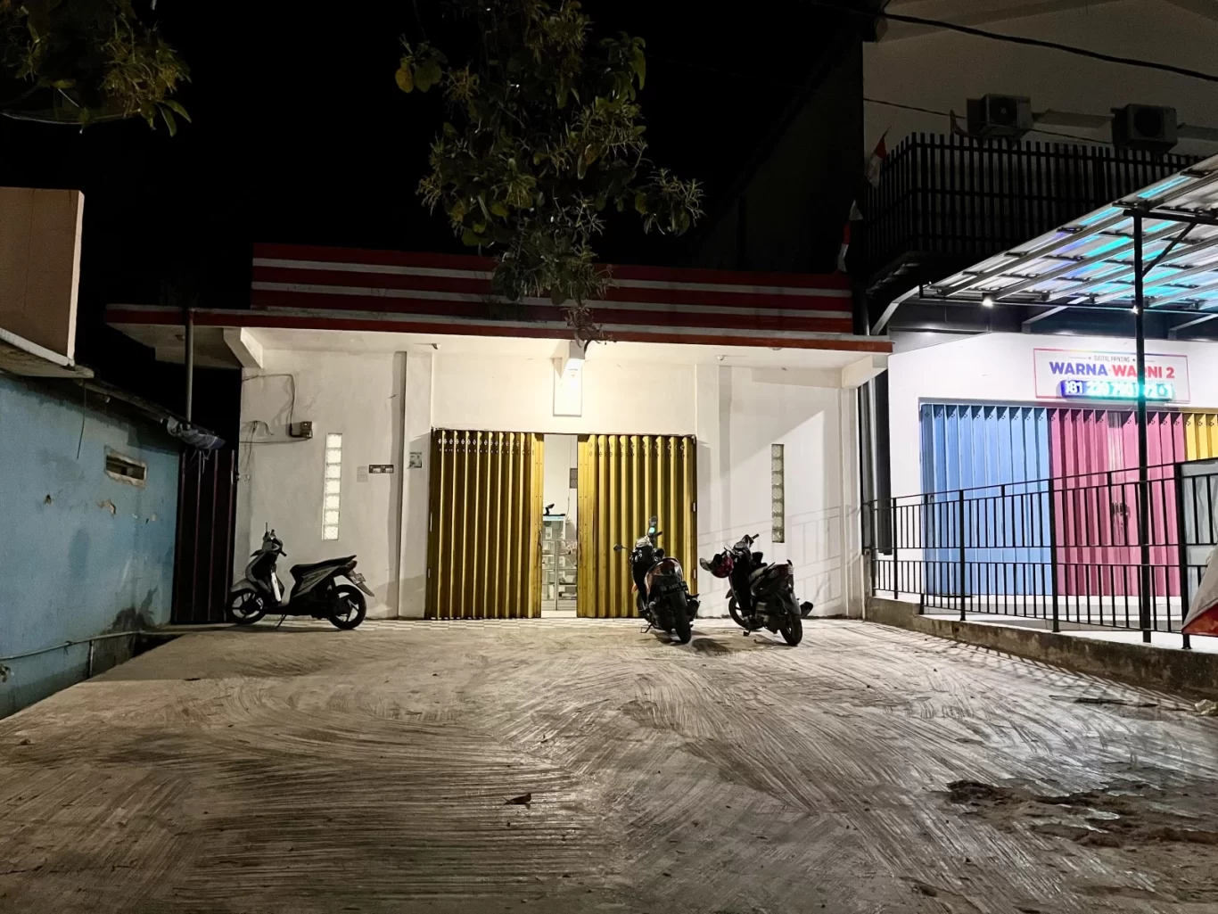 The exterior of Brownies Umma Uwais at night, showing its white facade, golden accordion doors, and three motorbikes on a concrete lot.