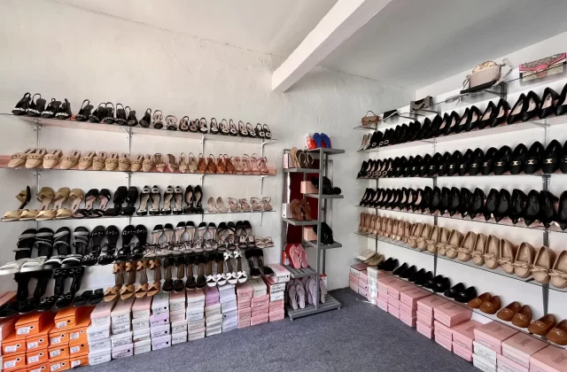 A brightly lit shoe store interior showcases rows of Valerie brand women's shoes, including heels, flats, and sandals, on glass shelves against white walls.