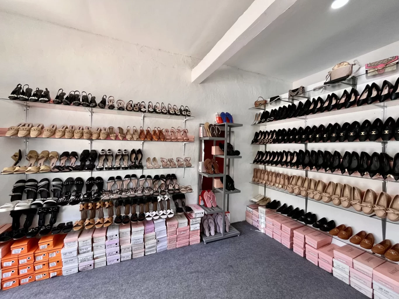 A brightly lit shoe store interior showcases rows of Valerie brand women's shoes, including heels, flats, and sandals, on glass shelves against white walls.