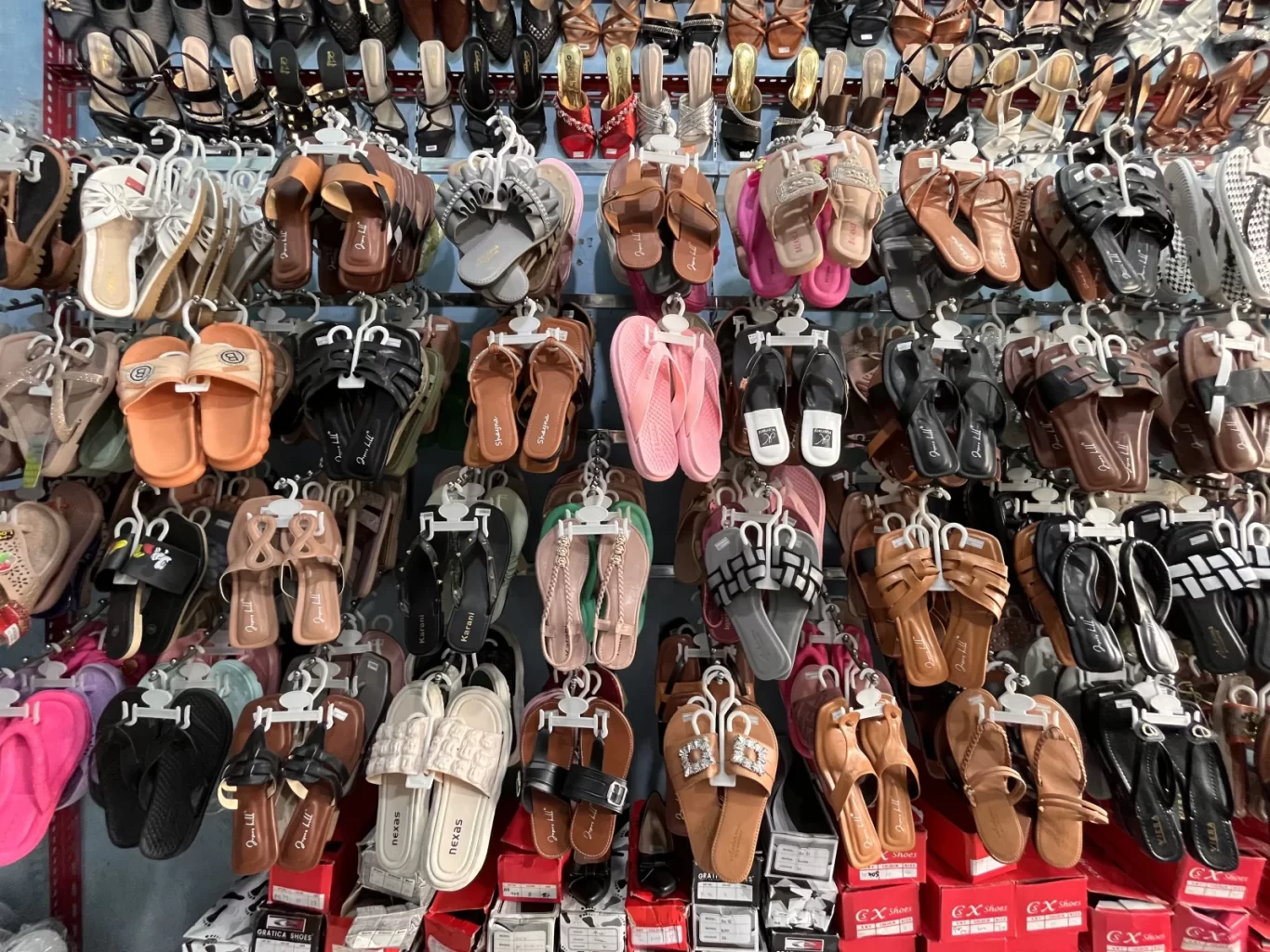 A wall display in Wahyu Store shows hundreds of sandals, flip-flops, and high heels in various colors and styles, hanging neatly on hooks.