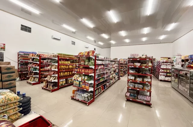 A brightly lit minimarket interior, Waimangura Pak Mart, with red-shelved aisles displaying a comprehensive selection of grocery items.