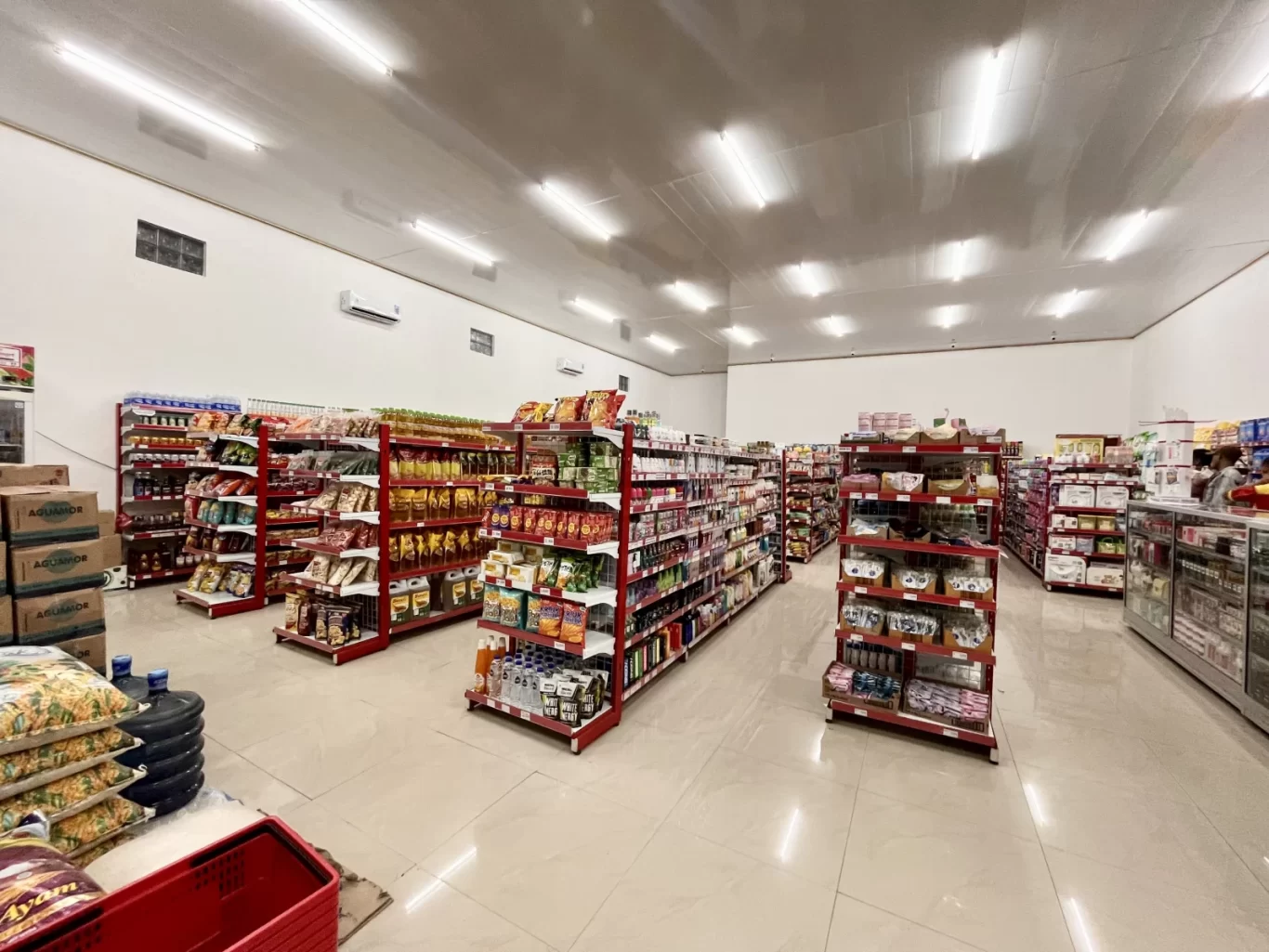 A brightly lit minimarket interior, Waimangura Pak Mart, with red-shelved aisles displaying a comprehensive selection of grocery items.