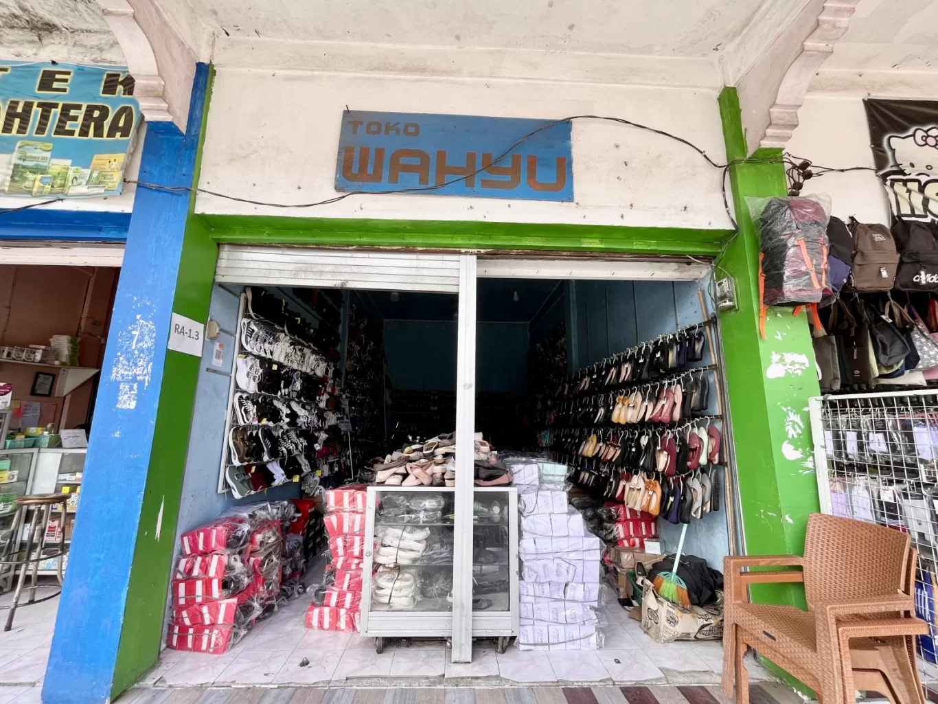 The storefront of Wahyu Store in Waikabubak, West Sumba, displays numerous shoes on racks and stacked boxes, with bags hanging on the right.