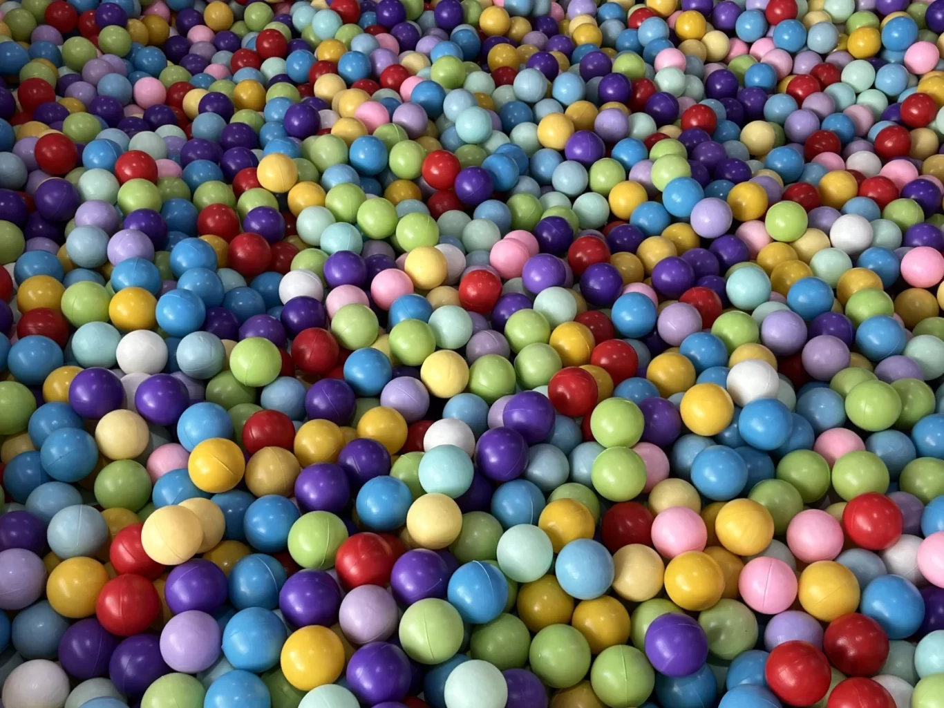 A vibrant ball pit is filled with countless small plastic balls in shades of red, blue, green, yellow, purple, and pink.