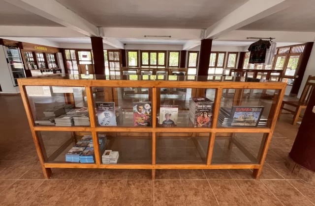 Interior of Rumah Budaya Sumba Souvenir Store, showing a wooden display case with books and items, surrounded by windows and more displays.