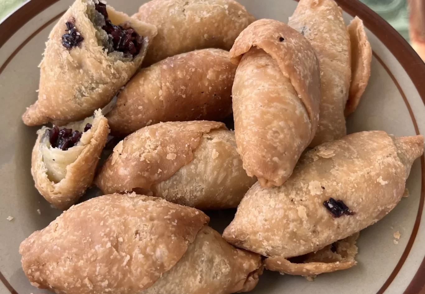 A close-up shows several golden-brown, crescent-shaped Molen pastries on a plate, with two broken open to reveal a dark sticky rice filling.