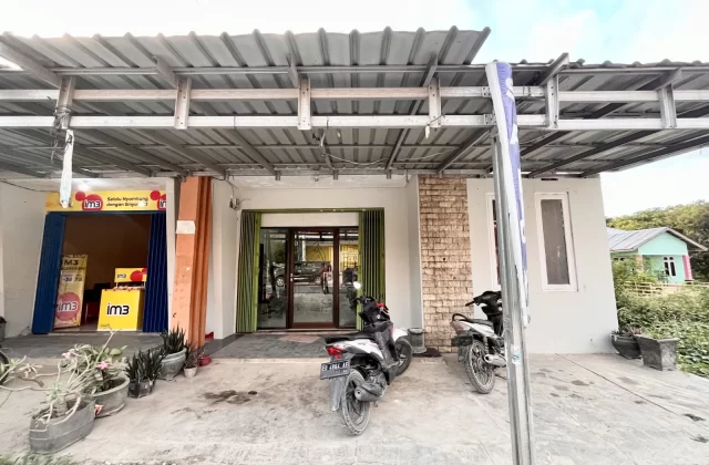 The exterior of Elsye Beauty Salon and an adjacent shop in Loura, Southwest Sumba, features light walls, green doors, and two parked motorbikes under a metal roof.