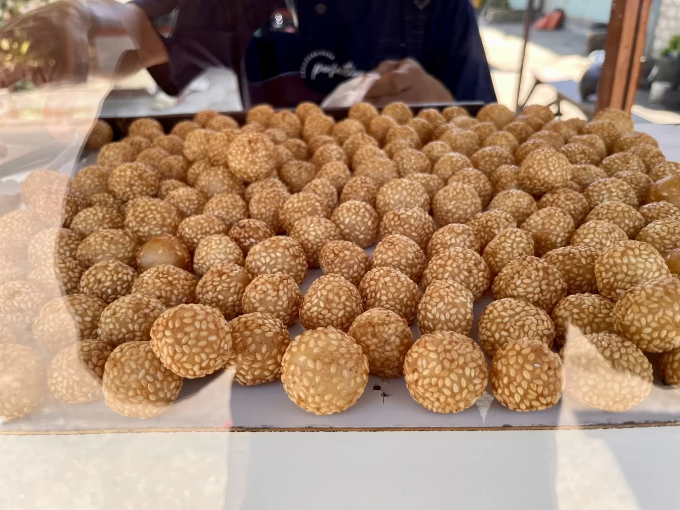 Hundreds of golden-brown, sesame-coated onde-onde, a traditional Indonesian sweet, are neatly arranged on a tray at a food stall.