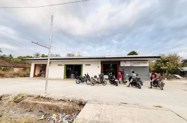 Valentine Digital Printing shop in Tambolaka, Sumba, with a white and grey facade, a wide concrete parking area, several motorbikes, and people.