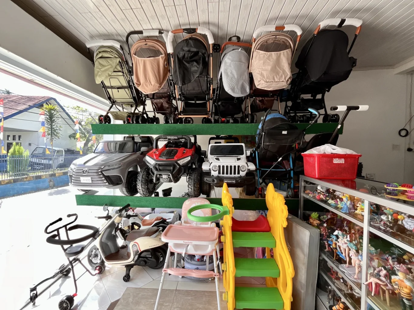 Inside Grace Toy Shop in Waikabubak, numerous colorful baby strollers, ride-on cars, and other children's toys are displayed on shelves and the floor.