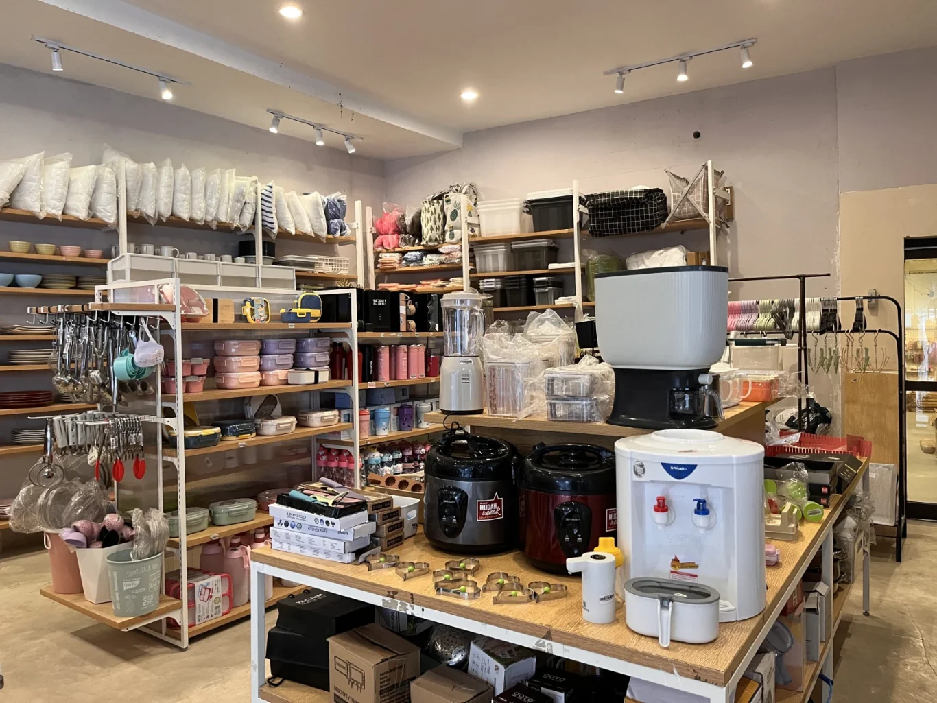 Interior of Kusuka Mura store in Waikabubak, displaying shelves filled with colorful kitchenware, storage containers, and small home appliances.