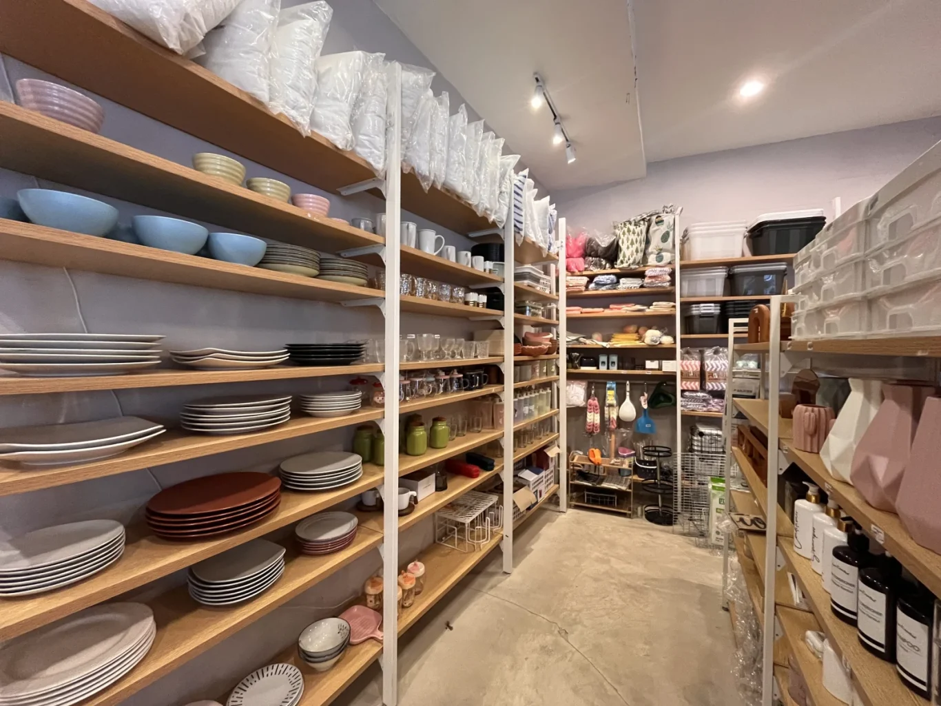 Inside Kusuka Mura, light wooden shelves display stacks of colorful plates, bowls, glasses, and various home goods in a well-lit retail space.