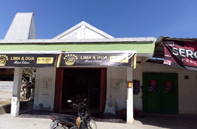 A small, white building with a green overhang features "LIMA & DUA" banners and an open entrance, with a black scooter parked outside under a clear blue sky.