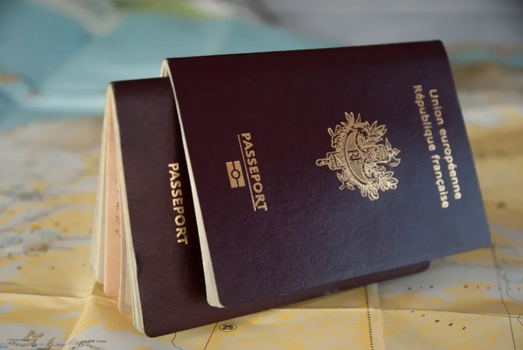Two dark red French passports with gold lettering rest on a light-colored map, one slightly open to reveal internal pages.